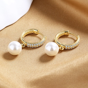 Macro detail of gold earrings featuring zircon inlay and a pendant white pearl