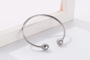 Macro shot of silver stainless steel open bangle with textured bead ends on white decor