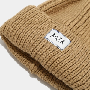 Close-up of caramel ribbed knit beanie with white AQER label showing fabric texture