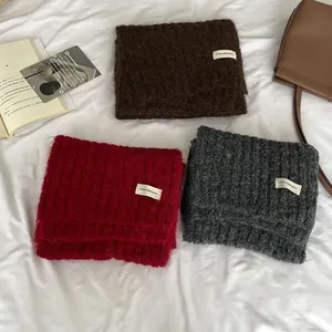 Detail of wool blend scarves in coffee, red and grey with knitted texture and fabric labels