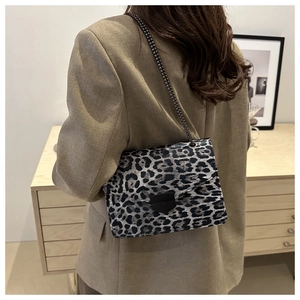 Detail of leopard print handbag with metallic clasp and chain strap worn on brown blazer
