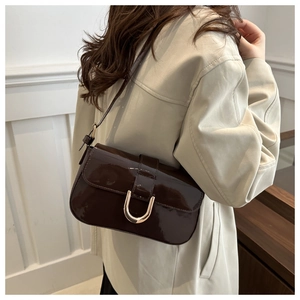 Detail view of dark brown patent leather shoulder bag with sleek metal horseshoe clasp