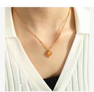 Détail du collier pendentif cœur avec perles dorées sur une chemise à rayures blanches