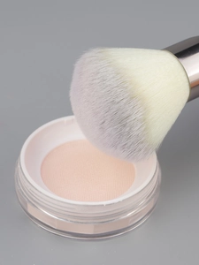 Macro shot of fluffy large powder brush with purple gradient bristles and loose face powder