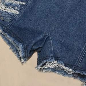 Détail d'un combishort en jean bleu avec déchirures et finitions à bords effilochés