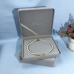 Detail of gray flocked jewelry box with pearl embroidery and pearl necklace inside