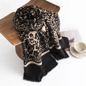 Leopard print pashmina scarf with fringe edges styled on a wooden chair with a coffee cup
