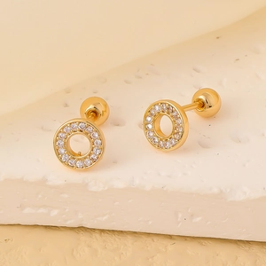 Macro shot of gold-plated stud earrings with white zircon on a stone texture background