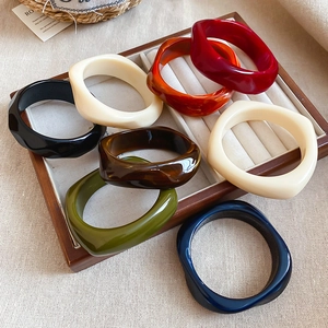 Detailed view of colorful twisted acrylic geometric bangles in a wooden jewelry tray