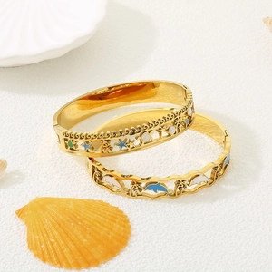 Goldenes Ozean-Armband mit Delphin und Palme Motiven auf weißem Hintergrund mit Muscheln