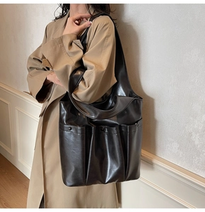 Detail of a large black PU leather tote bag with multi-pockets worn with a trench coat