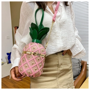 Detail of pink pineapple shoulder bag with gold rivets worn by a model in a cozy home setting