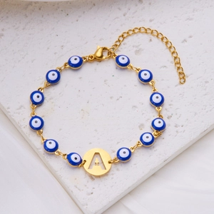 Detail of gold evil eye bracelet with blue enamel beads and round letter A pendant
