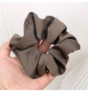 Close-up of a large brown satin scrunchie held by hand showing smooth silk texture
