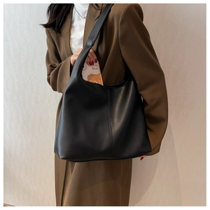 Fashionable black leather tote bag shown by model against a neutral wall background