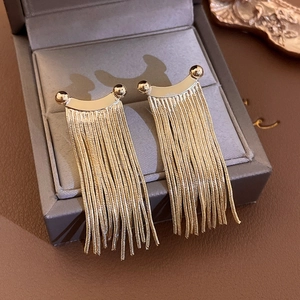 Close-up of golden fringe earrings with snake chains resting on a jewelry box