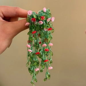 Detailed view of long handmade green beaded floral earrings with pink accents