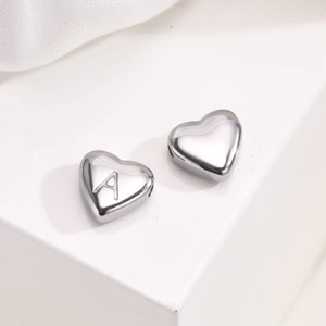 Macro detail of heart-shaped stainless steel beads showing engraved letter A and polished finish