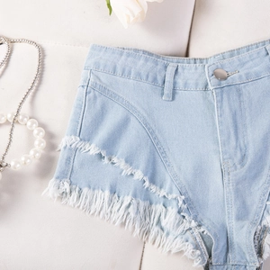 Dettaglio degli shorts in denim azzurro con bottone metallico e orlo sfrangiato con nappe