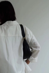 Minimalist black leather crescent bag with gold hardware shown on a model