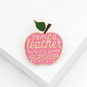 Macro shot of pink enamel apple teacher brooch with inspirational quote on white stand