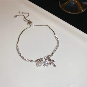 Detail of silver chain bracelet with zircon cross, star charms and white pearls