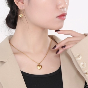 Gros plan d'une femme portant un ensemble de collier et boucles d'oreilles cœur dorés