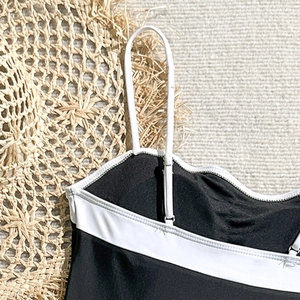 Detail of black swimsuit with white straps and contrast trim on textured background