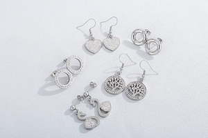 Macro shot of silver stainless steel earrings set with heart, tree of life, and swan motifs