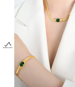 Detail of gold stainless steel snake chain set with oval green gemstones on a model