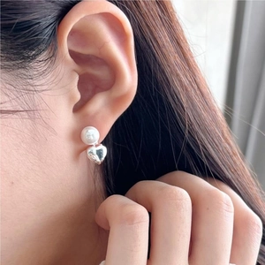 Detail of silver heart-shaped earring with white pearl on model's ear in close-up shot