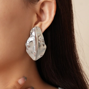 Macro shot of large irregular silver earrings with shell-like texture on a model side profile