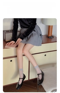 Detail of grey pleated skirt with black ribbon bow, paired with grey high-tube socks