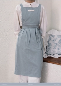 Detail of light blue cotton apron with waist ties shown on a model against a white wall