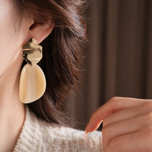Gros plan d'un mannequin portant des boucles d'oreilles irrégulières en acrylique or et beige