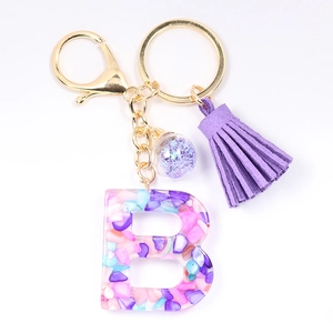 Detail of letter B crystal resin keychain with purple tassels and seashell fragments