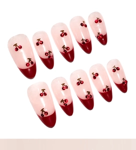 Detail of almond false nails with red French tips and 3D cherry rhinestone accents