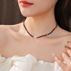 Detail of red garnet bead necklace with single white pearl on a model neck