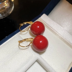 Close-up of luxury gold-plated earrings with vibrant red resin beads in a blue jewelry box