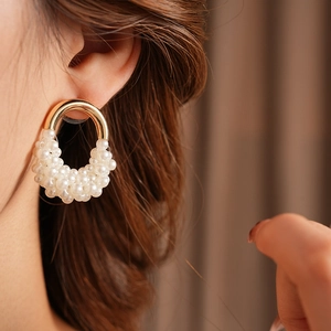 Dettaglio di orecchini dorati a forma di U con perle bianche indossati, stile retrò chic
