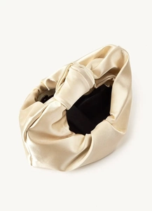 Detail of champagne gold satin clutch with elegant pleated design and knotted handle