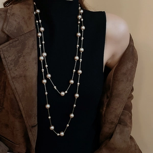 Double-layered pearl necklace with gold links worn over a black turtleneck sweater