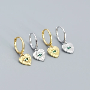 Detail of gold and silver heart hoop earrings with sunburst pattern and green gemstone