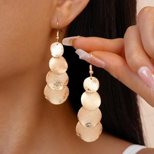Détail de boucles d'oreilles dorées mates avec quatre disques en métal texturé