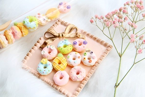 Nahaufnahme von bunten Harz-Donut-Anhängern mit Blumendesign auf rosa Tablett