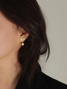 Close-up of golden hammered heart earrings with round embossed pendant on model