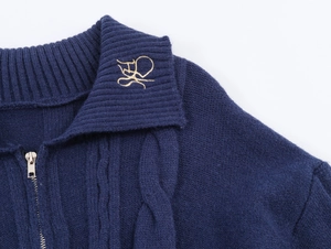Detail of navy cable knit cardigan showing gold embroidery on collar and metal zipper