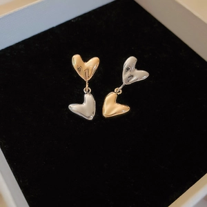 Two-tone heart-shaped earrings in gold and silver finish on a black velvet box