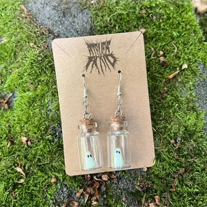 Luminous ghost necklace in a drift bottle on cardboard card with natural moss background