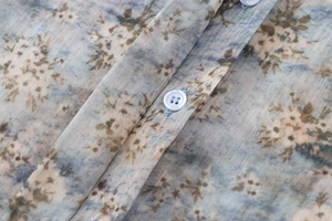 Détail du tissu en popeline bleu clair avec motif floral marron et boutons blancs